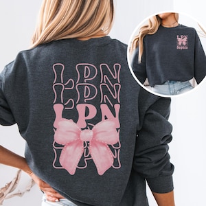 May include: A dark grey sweatshirt with a pink bow and the text "LPN" repeated three times. The sweatshirt has long sleeves and a crew neck.