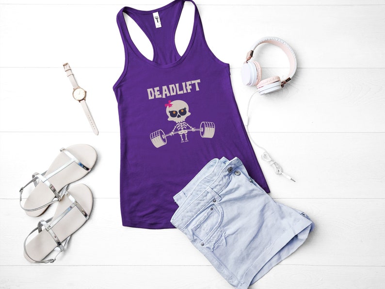May include: A purple racerback tank top with the word "DEADLIFT" above a skeleton lifting weights. The image also includes a pair of silver sandals, a watch, headphones, and denim shorts.