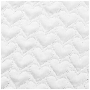 May include: Close-up of a white quilted fabric with a repeating heart pattern. The hearts are stitched in a diagonal pattern across the fabric, creating a textured surface. The stitching is a lighter shade of white.