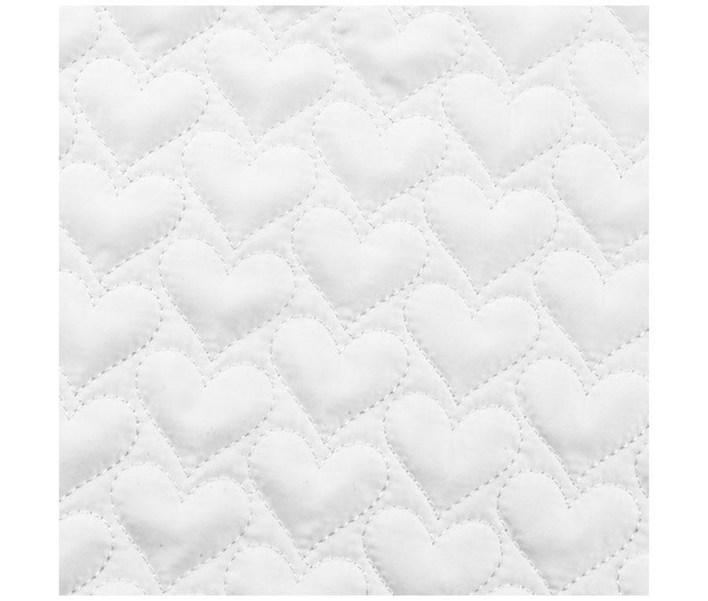 May include: Close-up of a white quilted fabric with a repeating heart pattern. The hearts are stitched in a diagonal pattern across the fabric, creating a textured surface. The stitching is a lighter shade of white.