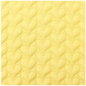 May include: Close-up of a yellow quilted fabric with a repeating heart pattern. The hearts are evenly spaced and outlined with stitching, creating a textured surface. The fabric has a soft, inviting appearance.