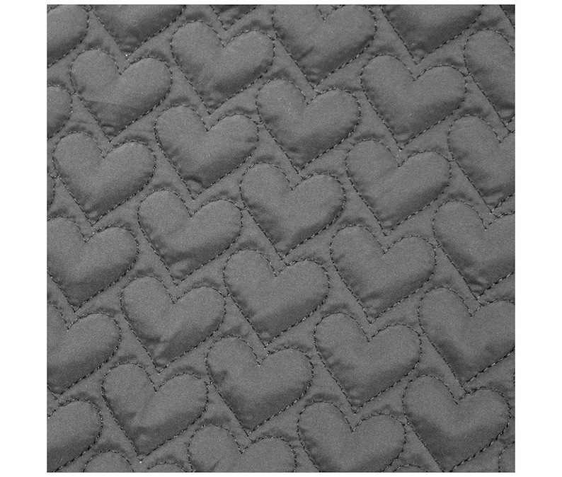 May include: Close-up of a gray quilted fabric with a repeating heart pattern. The hearts are stitched onto the fabric, creating a textured surface. The fabric is a solid gray color.
