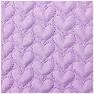 May include: Close-up of a lavender quilted fabric with a repeating heart pattern. The hearts are stitched with a contrasting thread, creating a textured effect. The fabric has a soft, padded appearance, suggesting a cozy textile.