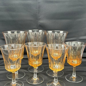 May include: A collection of eight vintage stemmed glasses. The glasses have a clear bowl with an amber-colored interior and a clear stem and base. The glasses are arranged on a dark surface.