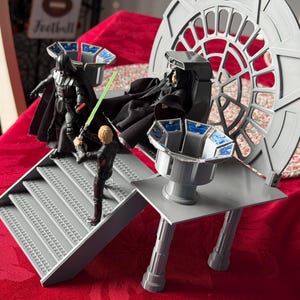 Può includere: Un playset a tema Star Wars con le figure di Darth Vader, Luke Skywalker e l'Imperatore Palpatine. Il set include una piattaforma grigia con scale, un trono e uno sfondo circolare. Darth Vader tiene una spada laser rossa e Luke Skywalker una spada laser verde.