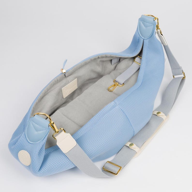 Peut inclure: Un sac de transport pour animaux de compagnie en maille bleu clair avec une sangle r&eacute;glable grise et blanche. Le sac a un fermoir en m&eacute;tal dor&eacute; et une doublure grise.