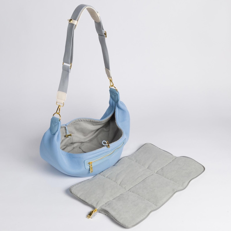 Peut inclure: Un sac &agrave; langer bleu clair avec une bandouli&egrave;re grise et blanche et un tapis &agrave; langer gris assorti. Le sac a une fermeture &eacute;clair et un tirette de fermeture &eacute;clair dor&eacute;e.