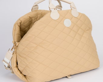 May include: A tan quilted travel bag with white leather handles and a white leather strap. The bag has a gold zipper and a white logo on the front.