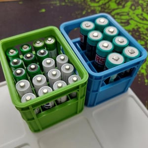 May include: Two plastic crates, one green and one blue, filled with AA batteries. The green crate has 24 batteries and the blue crate has 12 batteries.