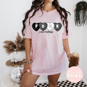 Könnte beinhalten: Ein überdimensioniertes rosa T-Shirt mit einer Grafik aus vier schwarzen und weißen Bonbonherzen, die "F U C K" buchstabieren, und dem Text "your feelings".