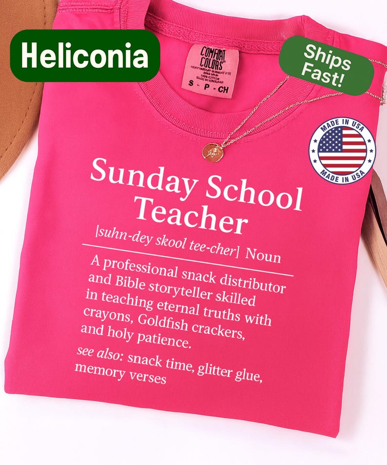 K&ouml;nnte beinhalten: Ein leuchtend pinkfarbenes T-Shirt mit dem Text "Sunday School Teacher" und einer Definition in Wei&szlig;. Eine goldene Halskette liegt auf dem T-Shirt. Der Markenname "Heliconia" wird oben links angezeigt.