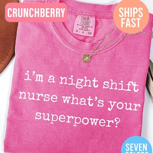 May include: A pink t-shirt with the text "i'm a night shift nurse what's your superpower?" in white. The shirt has a crew neck and a small gold necklace. The shirt is labeled "Crunchberry" and "Seven Colors".
