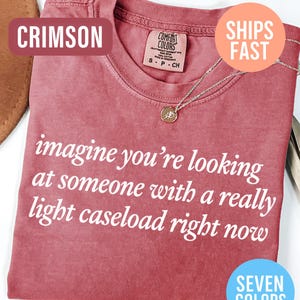 May include: Crimson-colored t-shirt with the text "imagine you're looking at someone with a really light caseload right now." The shirt has a crew neck and a small pendant necklace. The image also includes the text "Seven Colors."