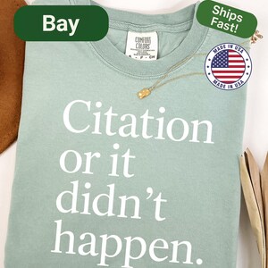 May include: A light green t-shirt with the text "Citation or it didn't happen" in white. The shirt has a crew neck and short sleeves. A gold necklace and a "Made in USA" sticker are also visible.