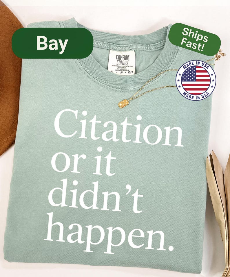 May include: A light green t-shirt with the text "Citation or it didn't happen" in white. The shirt has a crew neck and short sleeves. A gold necklace and a "Made in USA" sticker are also visible.