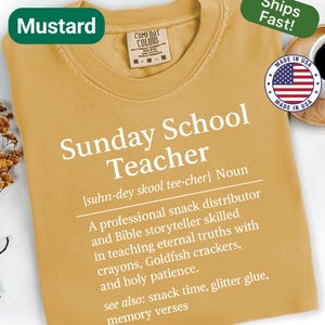 K&ouml;nnte beinhalten: Senffarbenes T-Shirt mit dem wei&szlig;en Text "Sunday School Teacher". Das Shirt enth&auml;lt eine Definition und eine Liste von Lehrerqualit&auml;ten. Ein gr&uuml;nes Etikett lautet "Mustard" und ein anderes "Ships Fast!"