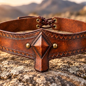 May include: A brown leather belt featuring a central diamond-shaped protrusion, two brass-colored studs, and embossed triangular patterns along the edges. The back includes a lace-up closure with brass-colored eyelets and brown leather cord.
