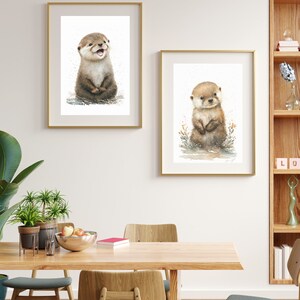 Op de afbeelding: Twee ingelijste aquarellen van otters. De otter in het linker schilderij zit rechtop en glimlacht. De otter in het rechter schilderij staat rechtop en kijkt naar de kijker. Beide otters zijn bruin en wit.