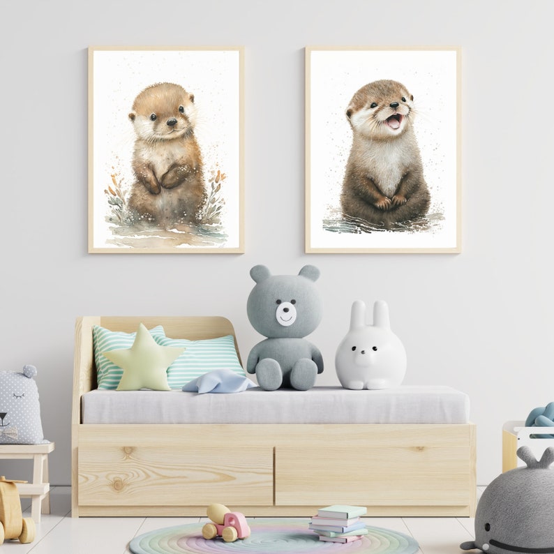 Op de afbeelding: Twee ingelijste aquarellen van schattige otters. De otters zijn bruin en wit en hebben grote ogen. De schilderijen zijn geplaatst tegen een witte muur met een houten bed en knuffels op de voorgrond.
