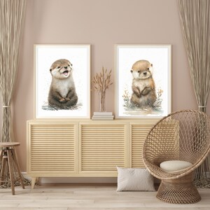 Op de afbeelding: Twee ingelijste aquarel illustraties van otters. De otter links glimlacht en zit rechtop. De otter rechts zit rechtop met gekruiste poten. Beide otters bevinden zich op een witte achtergrond.