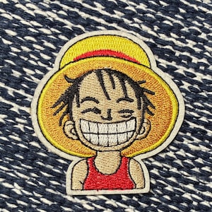 May include: Embroidered patch featuring a smiling cartoon character with a straw hat. The patch has a yellow and red color scheme, with black outlines and a white border. The character is wearing a red shirt.