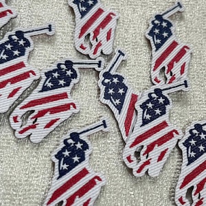 May include: A collection of embroidered patches featuring a polo player silhouette filled with the American flag pattern of red and white stripes and a blue field with white stars. The patches are textured with visible stitching throughout.