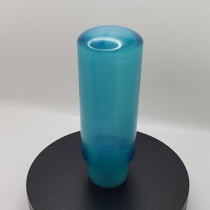 Op de afbeelding: Een cilindrisch, doorschijnend blauw object met een gladde, afgeronde bovenkant en een licht taps toelopende basis. Het object heeft een consistente, half-transparante azuurblauwe tint door de hele structuur en een gepolijste afwerking.