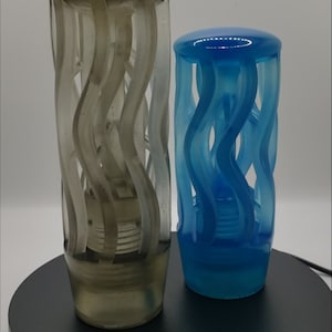 May include: Two cylindrical objects with a translucent finish, one in a smoky gray and the other in a vibrant blue. Each piece features a series of vertical, wavy, open-work structural elements that create a cage-like appearance around a central core.