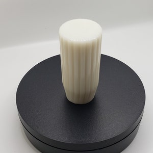 May include: A cylindrical off-white knob featuring a vertical ribbed texture along its sides and a smooth, flat circular top. The object is positioned upright, showcasing its uniform color and consistent fluted pattern throughout the exterior surface.