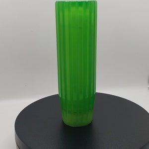 May include: A tall, cylindrical glass vase in a vibrant, translucent green hue. The exterior surface features a series of vertical, parallel ridges that run from the top rim down to the base, creating a consistent, repeating ribbed texture.