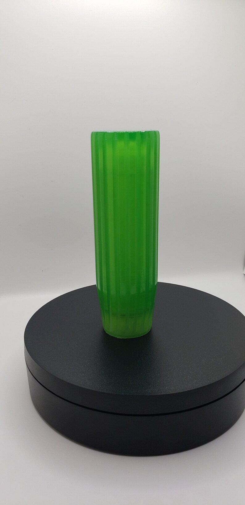 May include: A tall, cylindrical glass vase in a vibrant, translucent green hue. The exterior surface features a series of vertical, parallel ridges that run from the top rim down to the base, creating a consistent, repeating ribbed texture.