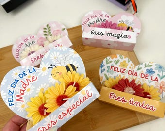May include: Three heart-shaped paper cards with attached artificial flowers and bee illustrations. The cards feature the text Feliz Día de la Madre, Eres especial, Eres magia, and Eres única in colourful script and block lettering.