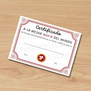 May include: A white certificate with a red border and decorative corner designs. The certificate has the words "Certificado A LA MEJOR NOVIA DEL MUNDO" in black text. A gold seal with a cupid is at the bottom.