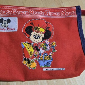 Może przedstawiać: Czerwona pł&oacute;cienna torba z grafiką Minnie Mouse. Torba przedstawia kresk&oacute;wkową Minnie Mouse trzymającą kwiaty i kosz. Tekst "Mouse Power" jest wydrukowany na g&oacute;rze i na małej naszywce. Krawędzie są obszyte niebieską tkaniną.