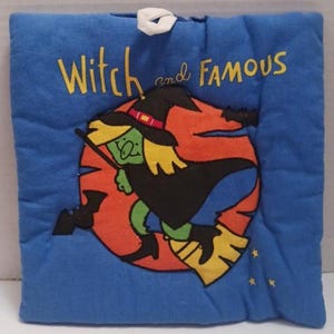 May include: Blue square Halloween-themed quilted wall hanging with the words "Witch and Famous" in yellow. The image features a cartoon witch on a broomstick against an orange background.