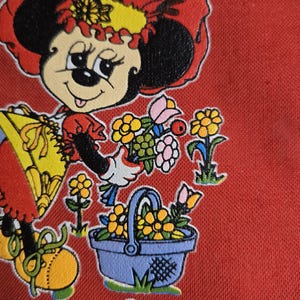 Może przedstawiać: Na czerwonym tle znajduje się ilustracja w stylu vintage przedstawiająca Minnie Mouse w czerwonym kapeluszu i sukience, trzymającą kwiaty i niebieski kosz wypełniony ż&oacute;łtymi kwiatami. Obraz zawiera tekst "&copy; WALT DISNEY PRODUCTIONS".