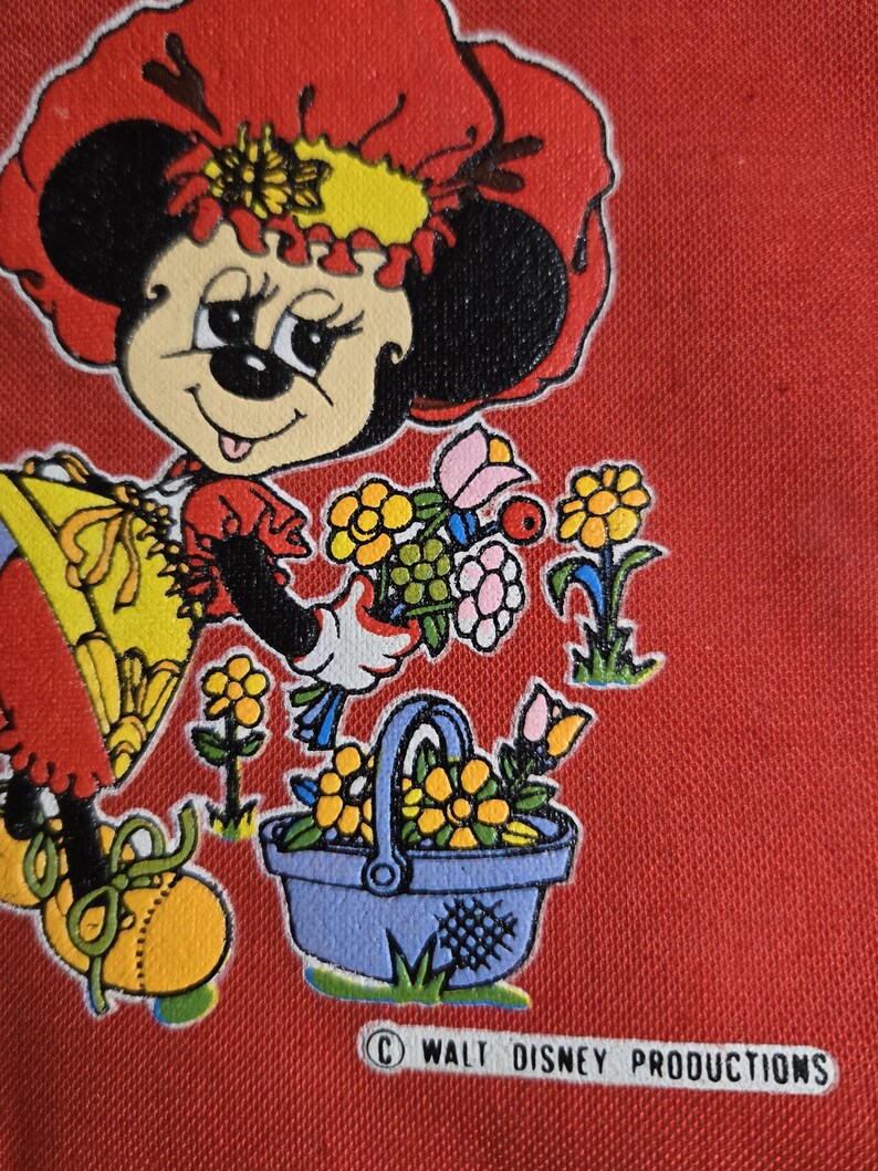 Może przedstawiać: Na czerwonym tle znajduje się ilustracja w stylu vintage przedstawiająca Minnie Mouse w czerwonym kapeluszu i sukience, trzymającą kwiaty i niebieski kosz wypełniony ż&oacute;łtymi kwiatami. Obraz zawiera tekst "&copy; WALT DISNEY PRODUCTIONS".