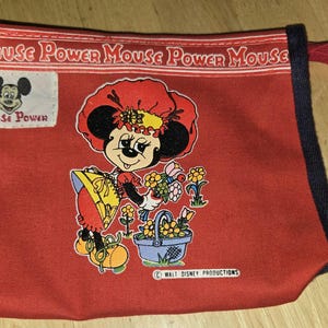 Może przedstawiać: Czerwona pł&oacute;cienna torba z grafiką Minnie Mouse i motywem kwiatowym. Torba ma czarne wykończenie i czerwony uchwyt. Tekst "Mouse Power" jest wydrukowany u g&oacute;ry. Widoczne jest logo Walt Disney Productions.
