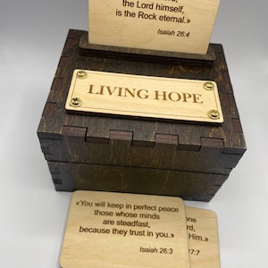 May include: A wooden box with a hinged lid, featuring the words "LIVING HOPE" on the front. The box is decorated with two small wooden plaques with inspirational quotes from the Bible, "Trust in the Lord forever, for the Lord, the Lord himself, is the Rock eternal." - Isaiah 26:4 and "You will keep in perfect peace those whose minds are steadfast, because they trust in you." - Isaiah 26:3.