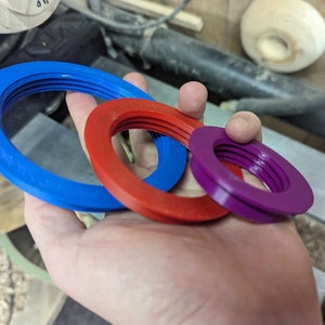 May include: Three different sized rings made of plastic. The rings are blue, red, and purple. The rings are stacked on top of each other.