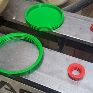 May include: Three 3D printed plastic rings, one green and two red. The green rings are larger and have a ridged texture. The red rings are smaller and have a smooth texture.