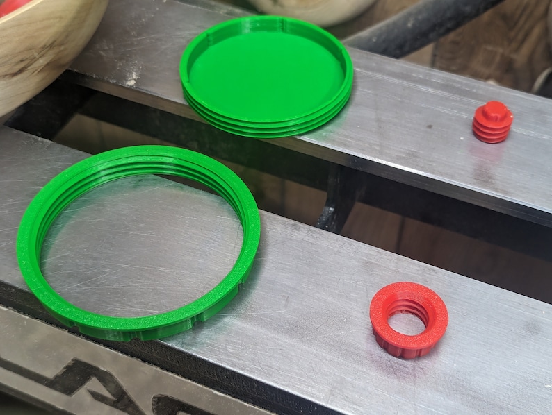 May include: Three 3D printed plastic rings, one green and two red. The green rings are larger and have a ridged texture. The red rings are smaller and have a smooth texture.