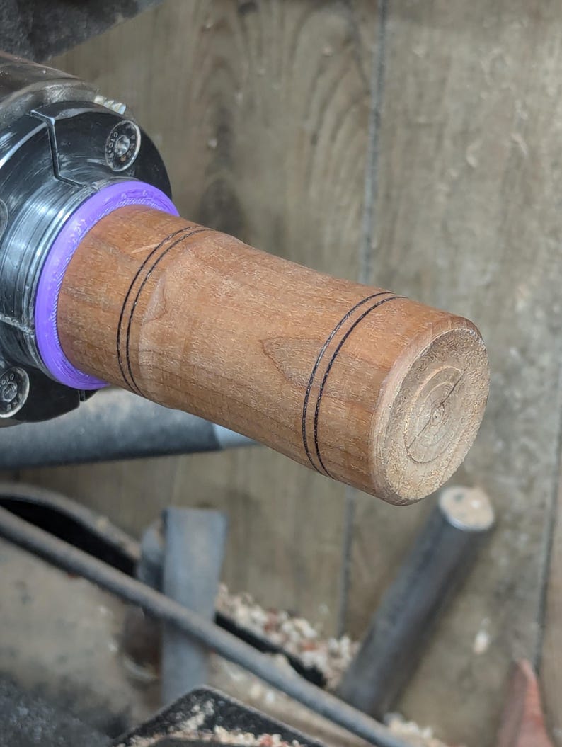 May include: A close-up of a wooden handle with two black lines around the center. The handle is being turned on a lathe.