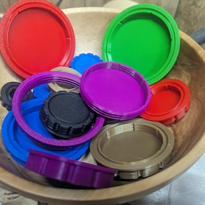 May include: A collection of colorful plastic lids in a wooden bowl. The lids are in various shades of red, green, purple, blue, and brown.