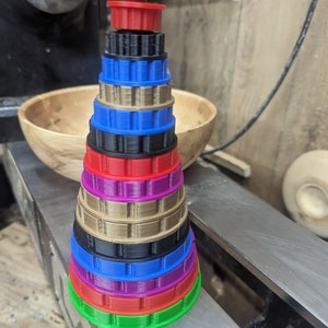 May include: A stack of colorful plastic rings, each with a different pattern, arranged in a cone shape. The rings are green, red, black, blue, gold, purple, and red.
