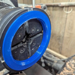 May include: Close-up of a blue and black lathe chuck with four jaws. The jaws are open and ready to hold a piece of wood.