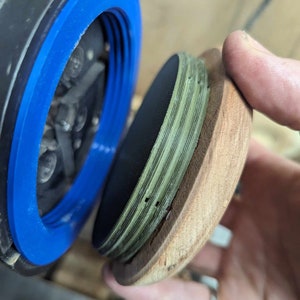 May include: A close-up of a wooden lid with a green and black layered design. The lid is being held by a hand and is being placed on top of a black and blue object.