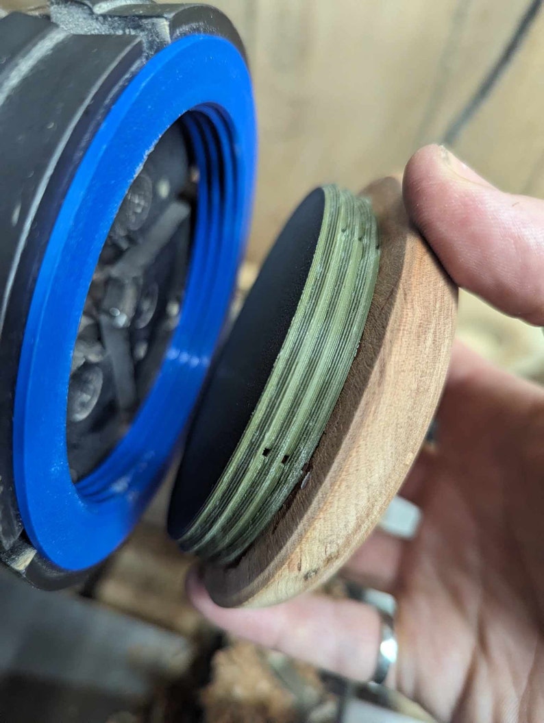 May include: A close-up of a wooden lid with a green and black layered design. The lid is being held by a hand and is being placed on top of a black and blue object.