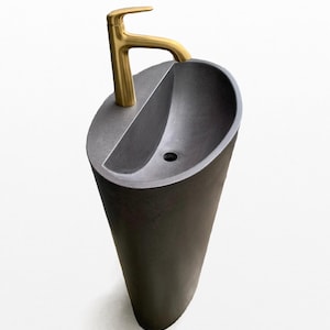 May include: A black pedestal sink with a gold faucet. The sink is oval shaped and has a single hole for the faucet. The sink is made of a smooth, polished material.