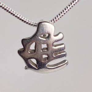 May include: A silver-toned pendant featuring a stylized, cut-out Japanese kanji character suspended from a thin, matching silver-toned snake chain. The pendant has a polished metallic finish and an intricate, open-work design with smooth edges.